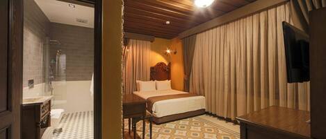 A hotel room with a bed, a desk, a television, and a bathroom visible through an open door.