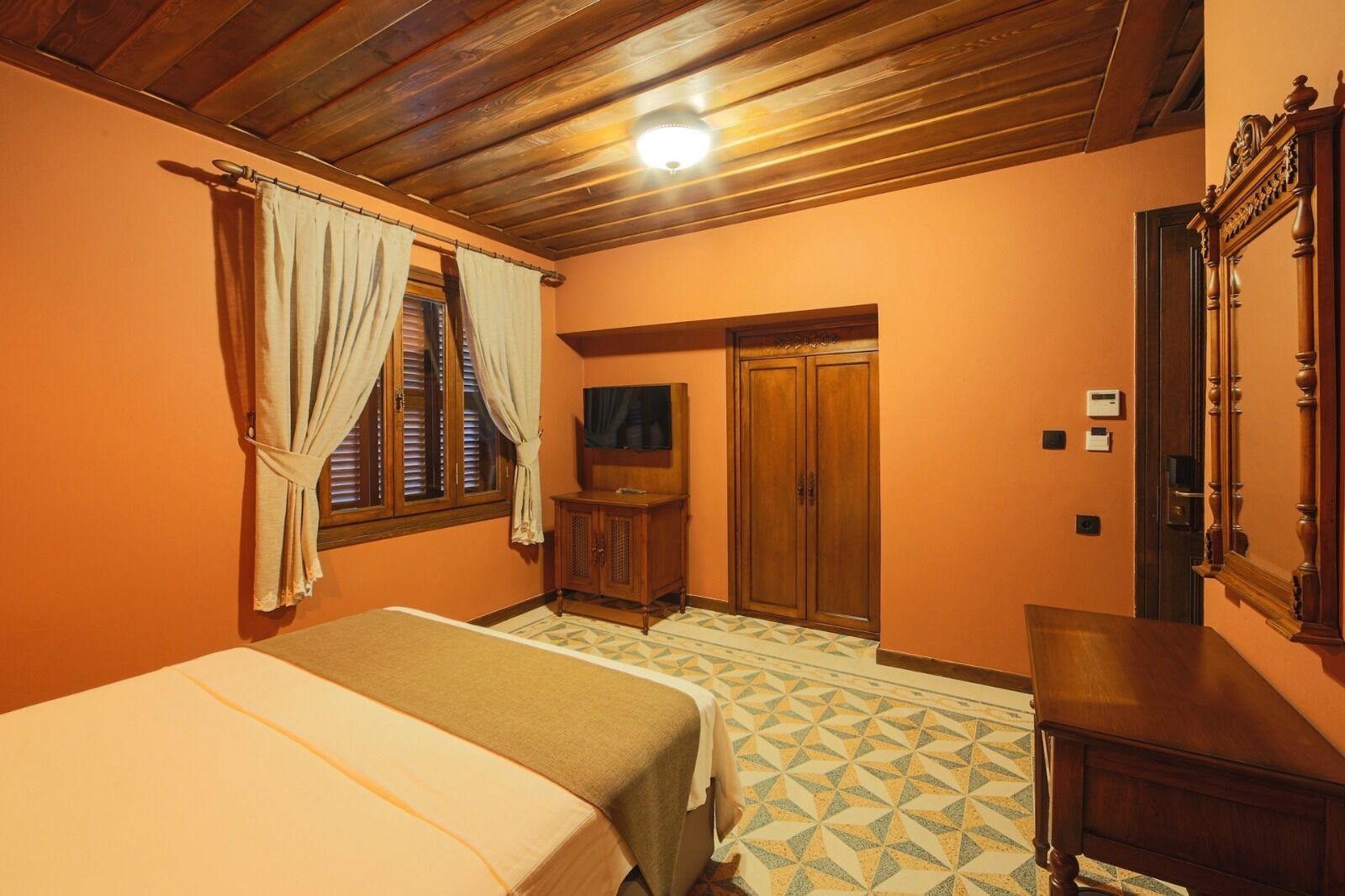 A bedroom with a bed, a wooden wardrobe, a television, and a door leading to another room.