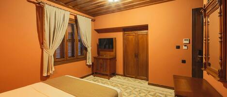 A bedroom with a bed, a wooden wardrobe, a television, and a door leading to another room.