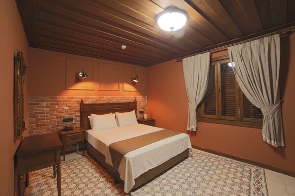 A bedroom with a brick-patterned headboard, a bed with white linens, a nightstand, a wall-mounted lamp, and a window with curtains. - Sam Franss Boutique Otel (Antakya)