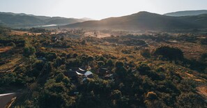 Vista aérea de una zona rural con casas dispersas, rodeadas de vegetación densa y colinas al fondo.