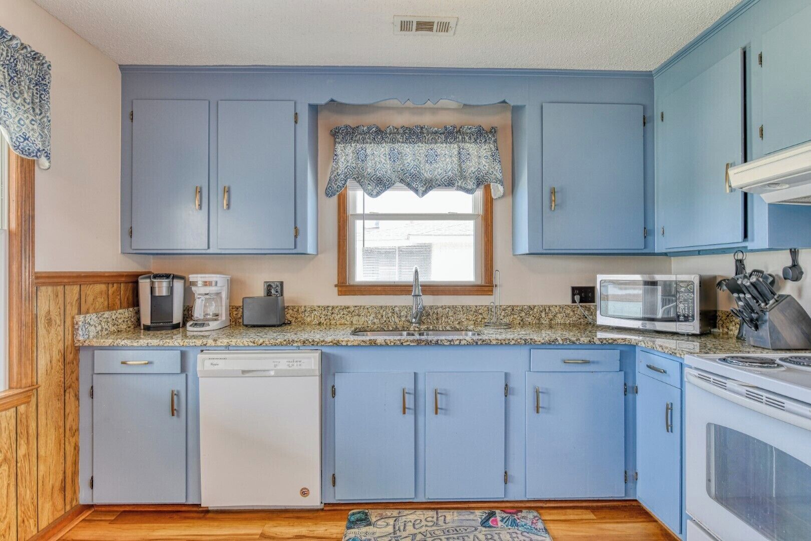 A kitchen with blue cabinets, a granite countertop, a dishwasher, a coffee maker, a toaster, a microwave, and a stove.