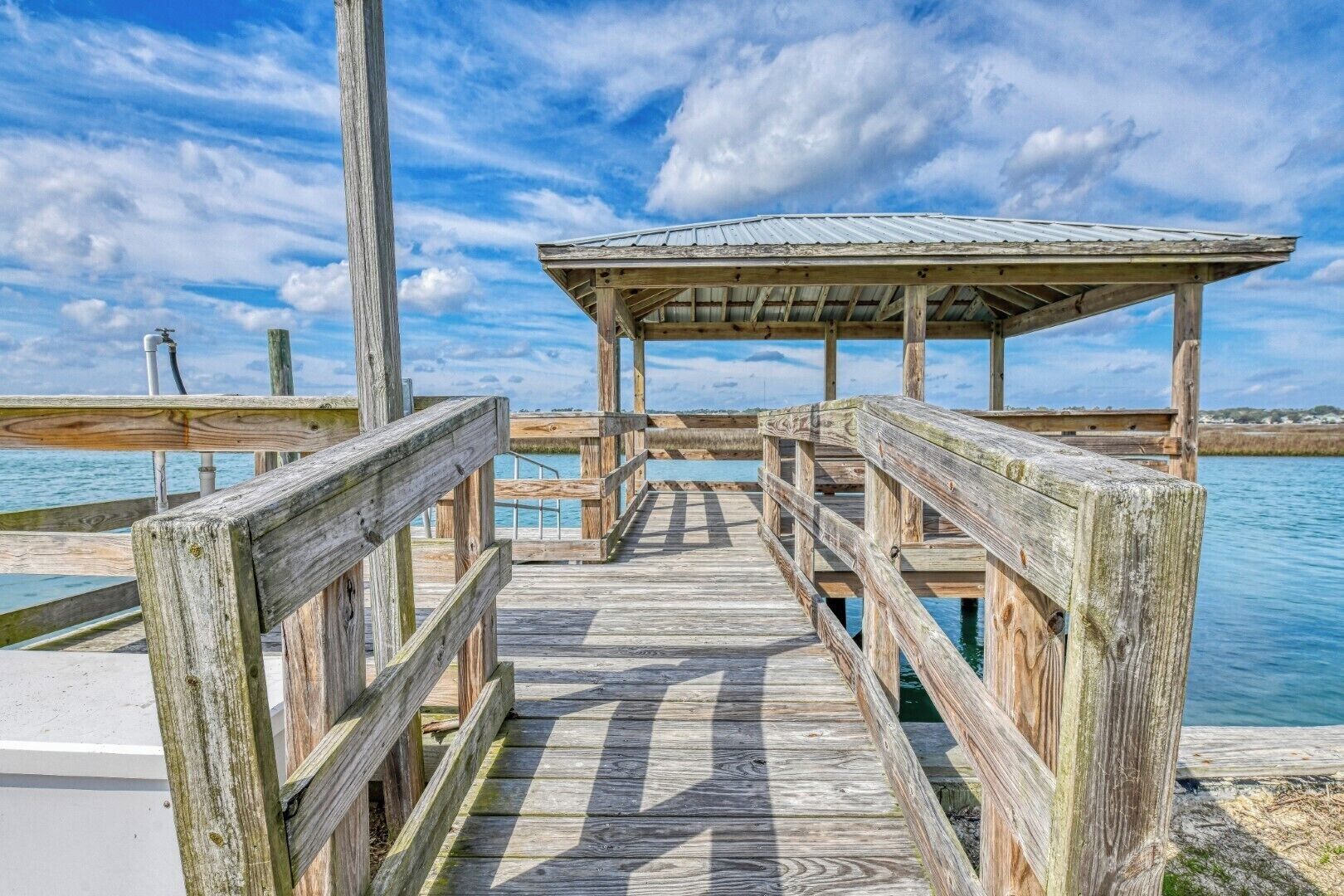 A wooden pier leading to a covered area with a metal roof, extending into a body of water.