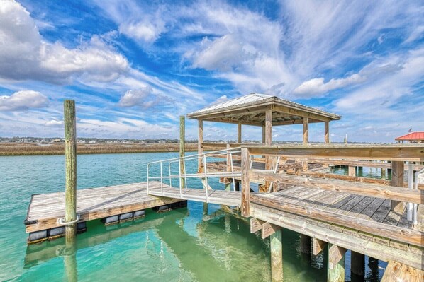 A wooden pier with a covered seating area extending into a body of water, surrounded by a clear sky.