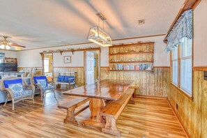 A spacious living area with a wooden dining table, wicker chairs, and a bookshelf filled with books and decorative items.