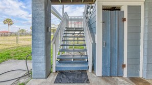 A covered outdoor staircase leading to a house with a blue door and a concrete pillar on the left. - Inlet Joy 2nd Row Channel Front (Garden City Beach)