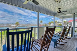 A covered porch with wooden chairs and a table, overlooking a body of water and distant buildings. - Inlet Joy 2nd Row Channel Front (Garden City Beach)