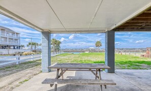 A covered picnic area with a concrete table and benches, overlooking a grassy field and a body of water.