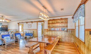 A spacious room with a wooden dining table, wicker chairs, a television, and a bookshelf.