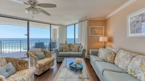 A spacious living area with a balcony overlooking the sea, furnished with a sofa, armchairs, and a coffee table.