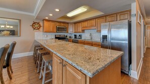 A modern kitchen with granite countertops, stainless steel appliances, wooden cabinets, and a bar area with stools.
