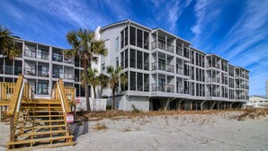 Un hôtel situé en bord de mer, doté de nombreux balcons, d’une terrasse en bois et d’une plage de sable.
