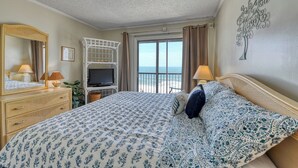 Une chambre d’hôtel avec un grand lit, une télévision, une commode et un balcon offrant une vue sur l’océan.
