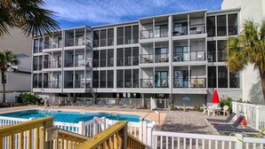 Un hôtel à plusieurs étages doté de balcons, d’une piscine et d’un espace extérieur aménagé pour s’asseoir.