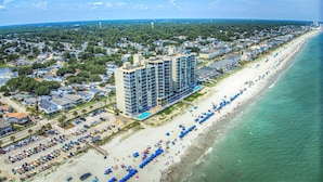 A coastal hotel with multiple floors, a beachside location, and a parking lot with numerous vehicles. - One Ocean Place 403 - Fantastic two-bedroom, two-bath oceanfront condo in GCB (Garden City Beach)