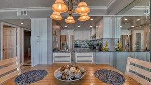 A modern kitchen with white cabinets, a stainless steel refrigerator, and a dining table with decorative bowls. - One Ocean Place 403 - Fantastic two-bedroom, two-bath oceanfront condo in GCB (Garden City Beach)