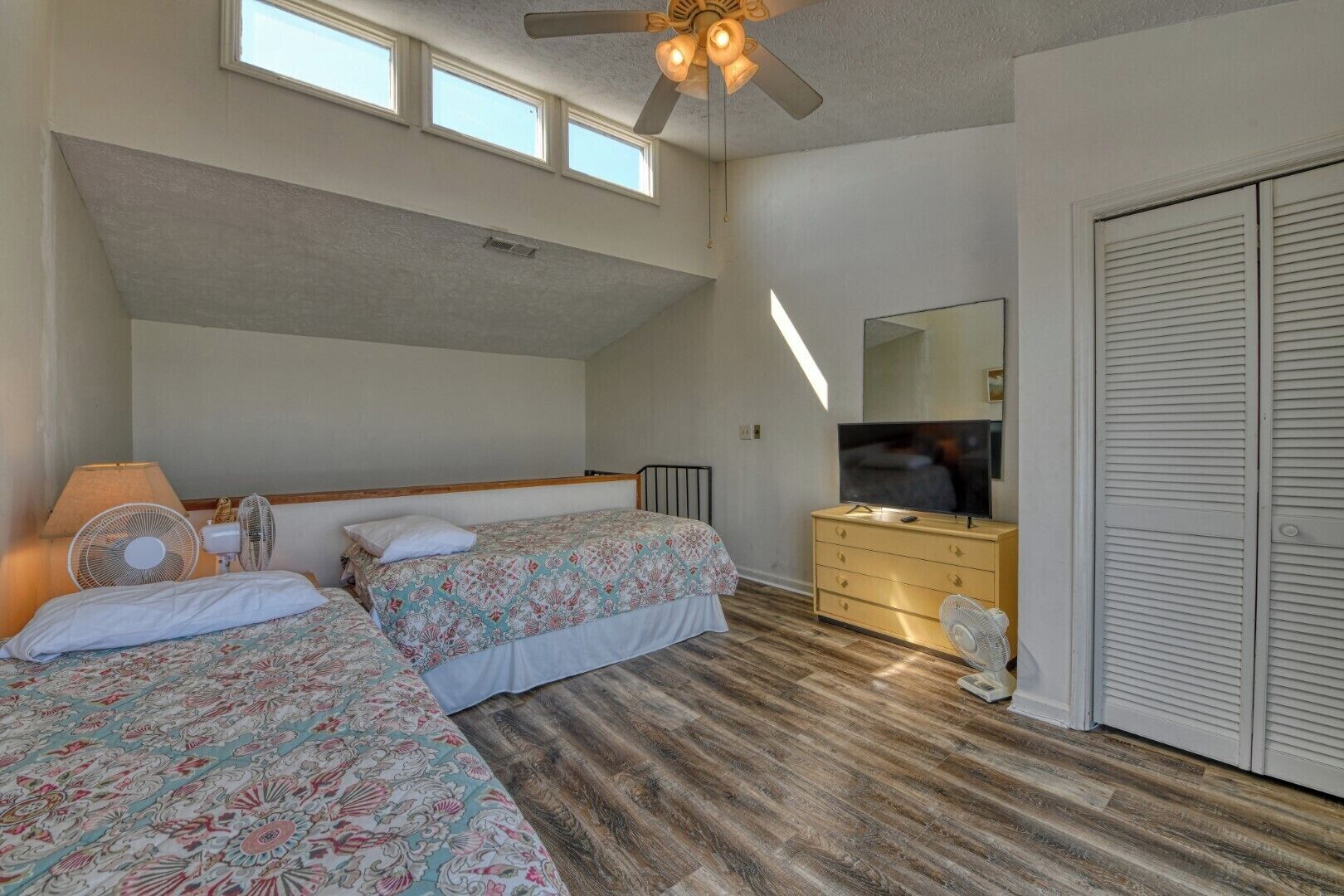 Une chambre avec deux lits, une commode, un téléviseur et un ventilateur de plafond.