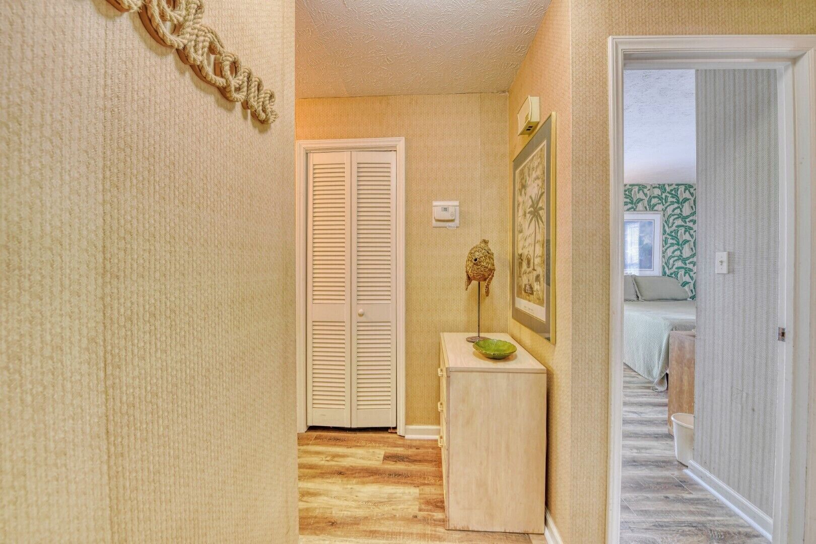 A narrow hallway with a wooden floor, a white door, and a small table with a green bowl and a decorative item.