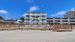 Un hôtel situé en bord de mer, doté de nombreux balcons, d’une clôture en bois et d’une plage de sable.
