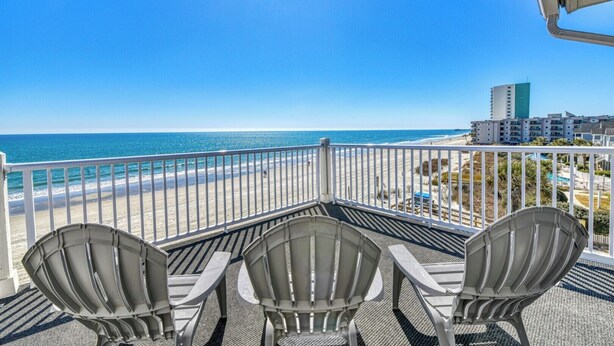 Un balcon avec trois fauteuils Adirondack donnant sur une plage et l’océan.
