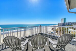 Ein Balkon mit drei Adirondack-Stühlen mit Blick auf einen Strand und das Meer.