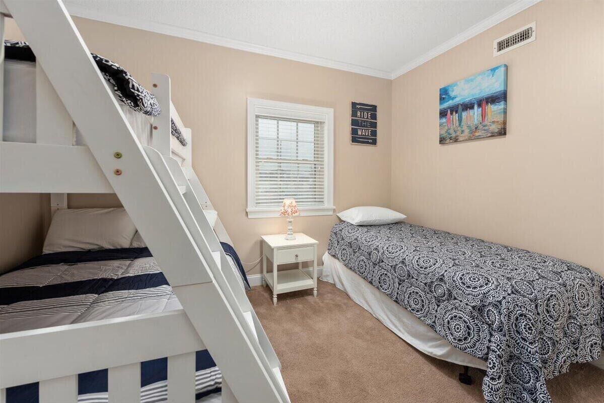 Ein Schlafzimmer mit Etagenbett, einem Einzelbett, einem Nachttisch mit Lampe, einem Fenster mit Jalousien und einem Bild an der Wand.