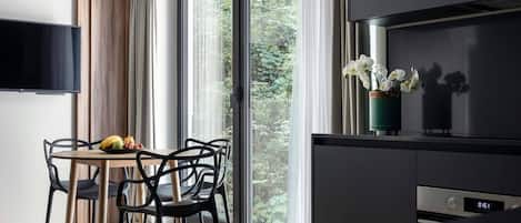 A modern kitchen with a built-in oven, a dining area with a table and chairs, and a large window with a view of greenery.