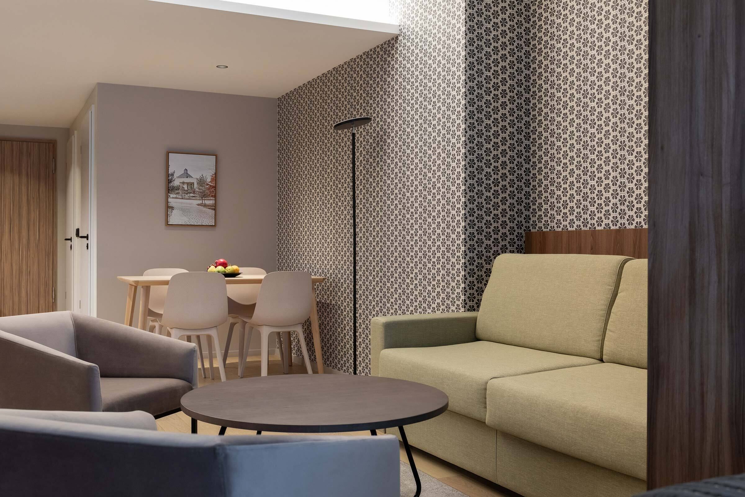 Ein modernes Wohnzimmer mit einer Couch, zwei Sesseln, einem runden Couchtisch und einem Essbereich mit Tisch und Stühlen.