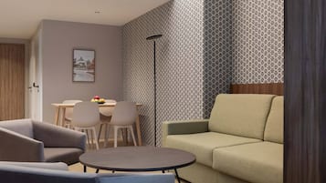 Ein modernes Wohnzimmer mit einer Couch, zwei Sesseln, einem runden Couchtisch und einem Essbereich mit Tisch und Stühlen.