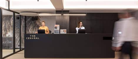 A reception desk with two staff members, a modern interior, and a glass wall.