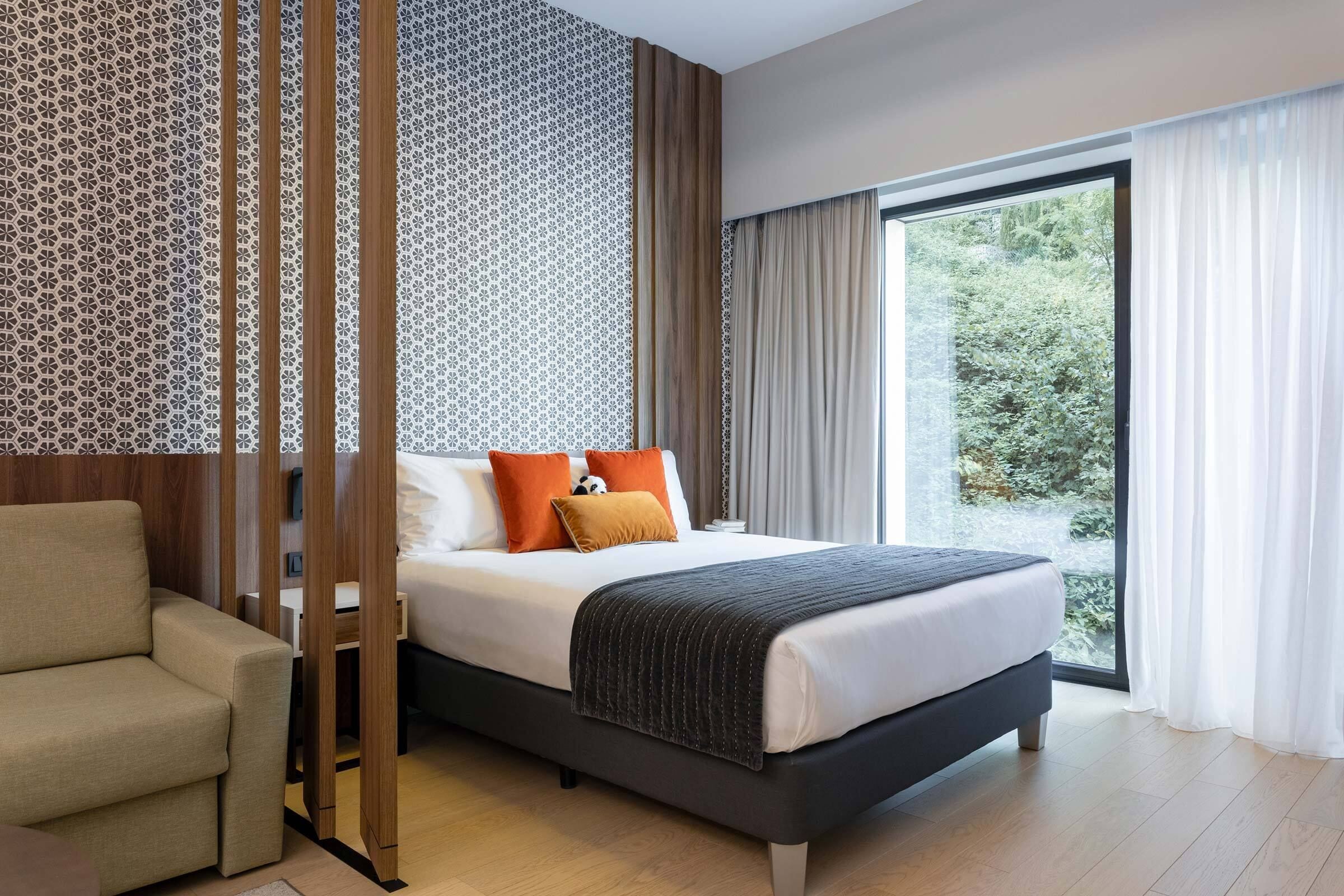 Una habitación de hotel moderna con una cama grande, un sofá y vistas a la vegetación por la ventana.