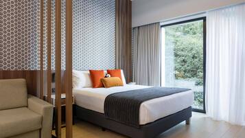 Una habitación de hotel moderna con una cama grande, un sofá y vistas a la vegetación por la ventana.