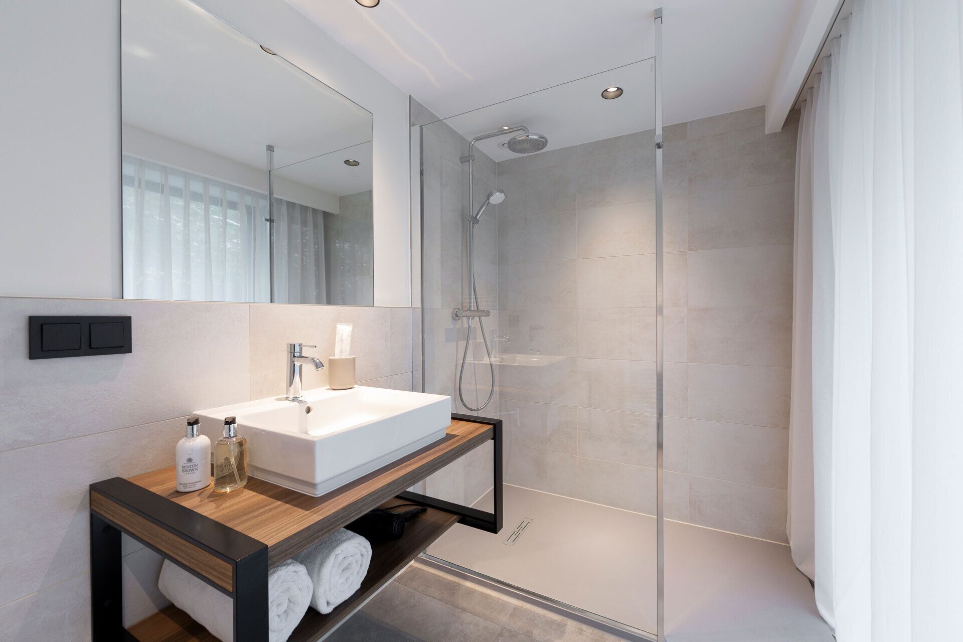 Un baño moderno con cabina de ducha de vidrio, un lavabo blanco y un mueble de tocador de madera.