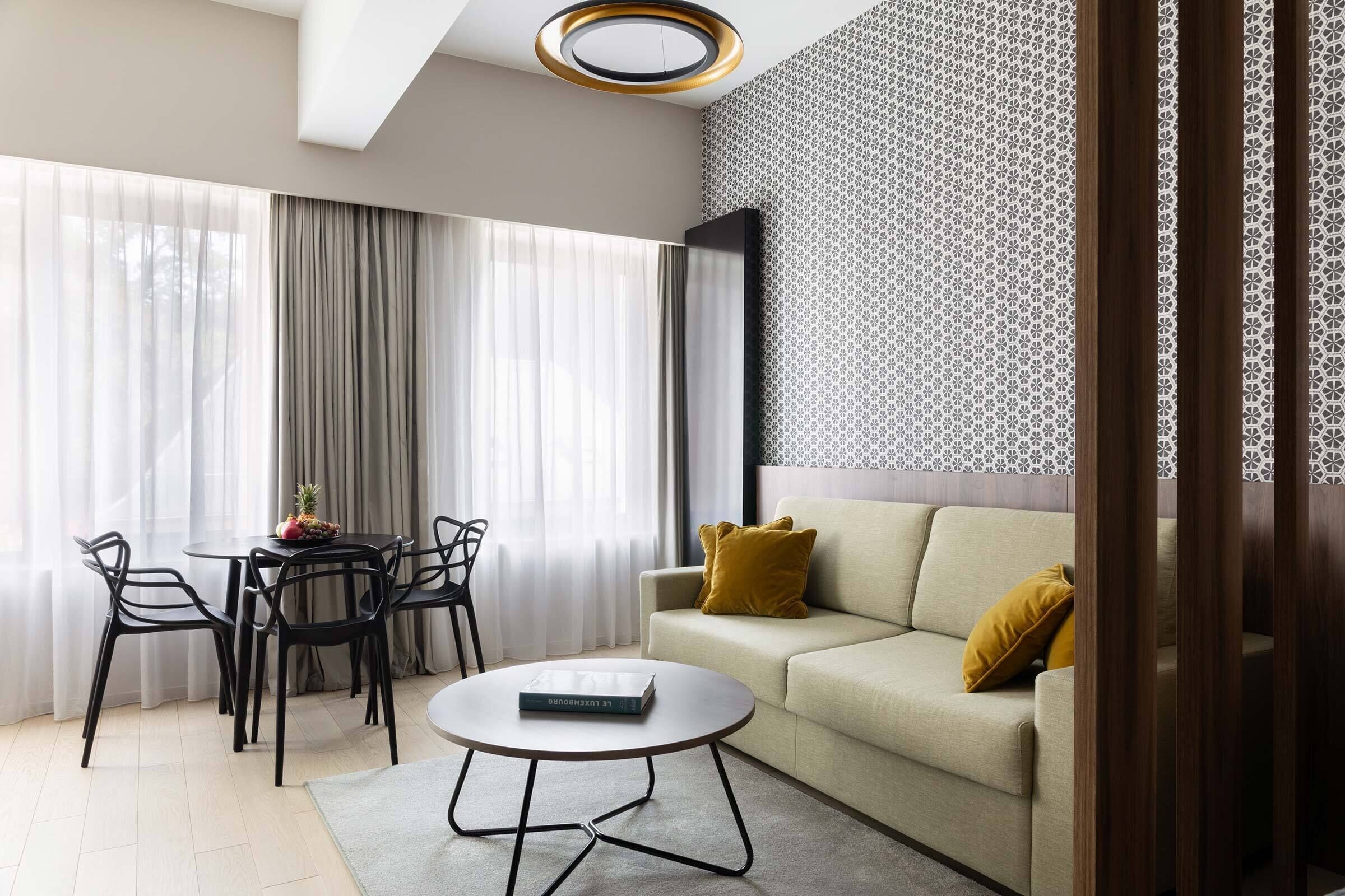 Ein modernes Wohnzimmer mit einer Couch, einem Couchtisch, einem Esstisch mit Stühlen und einer Wand mit Muster.
