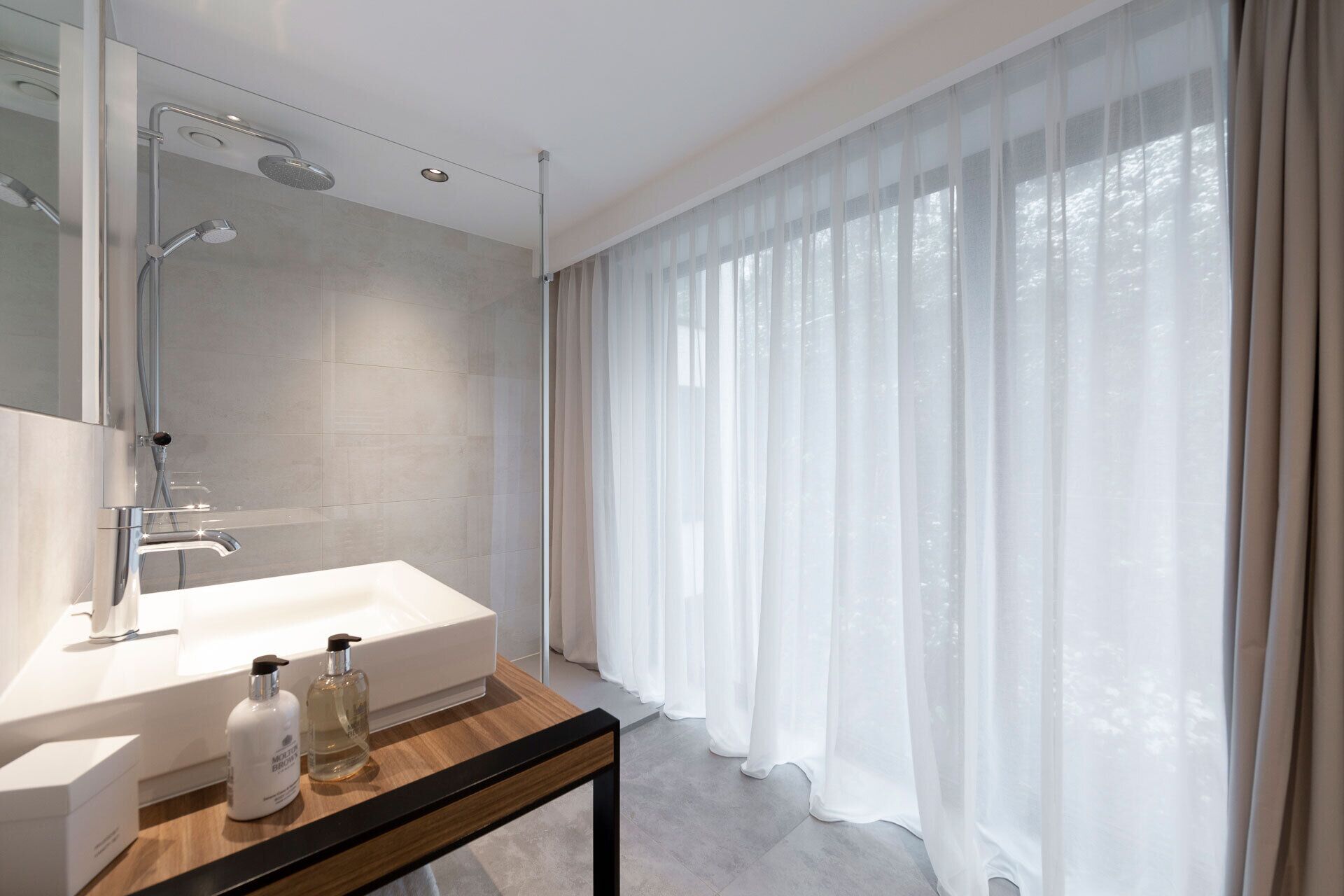 A modern bathroom with a large shower, a white sink, and a bottle of shampoo.