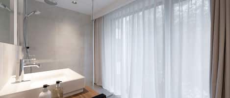 Een moderne badkamer met een ruime douche, een wit wastafeltje en een fles shampoo.