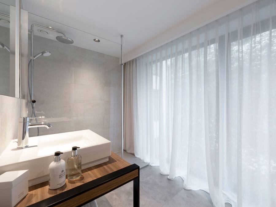 A modern bathroom with a large shower, a white sink, and a bottle of shampoo.