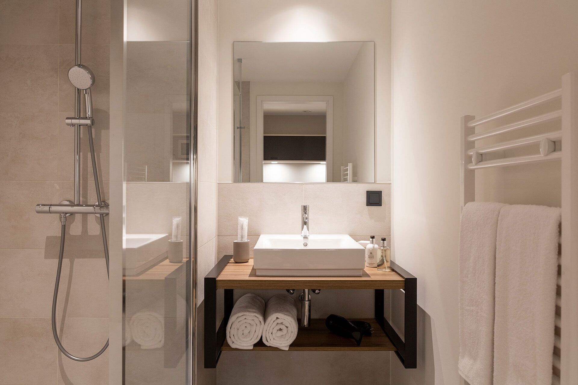 A modern bathroom with a glass-enclosed shower, a wooden vanity with a sink, and a towel rack.