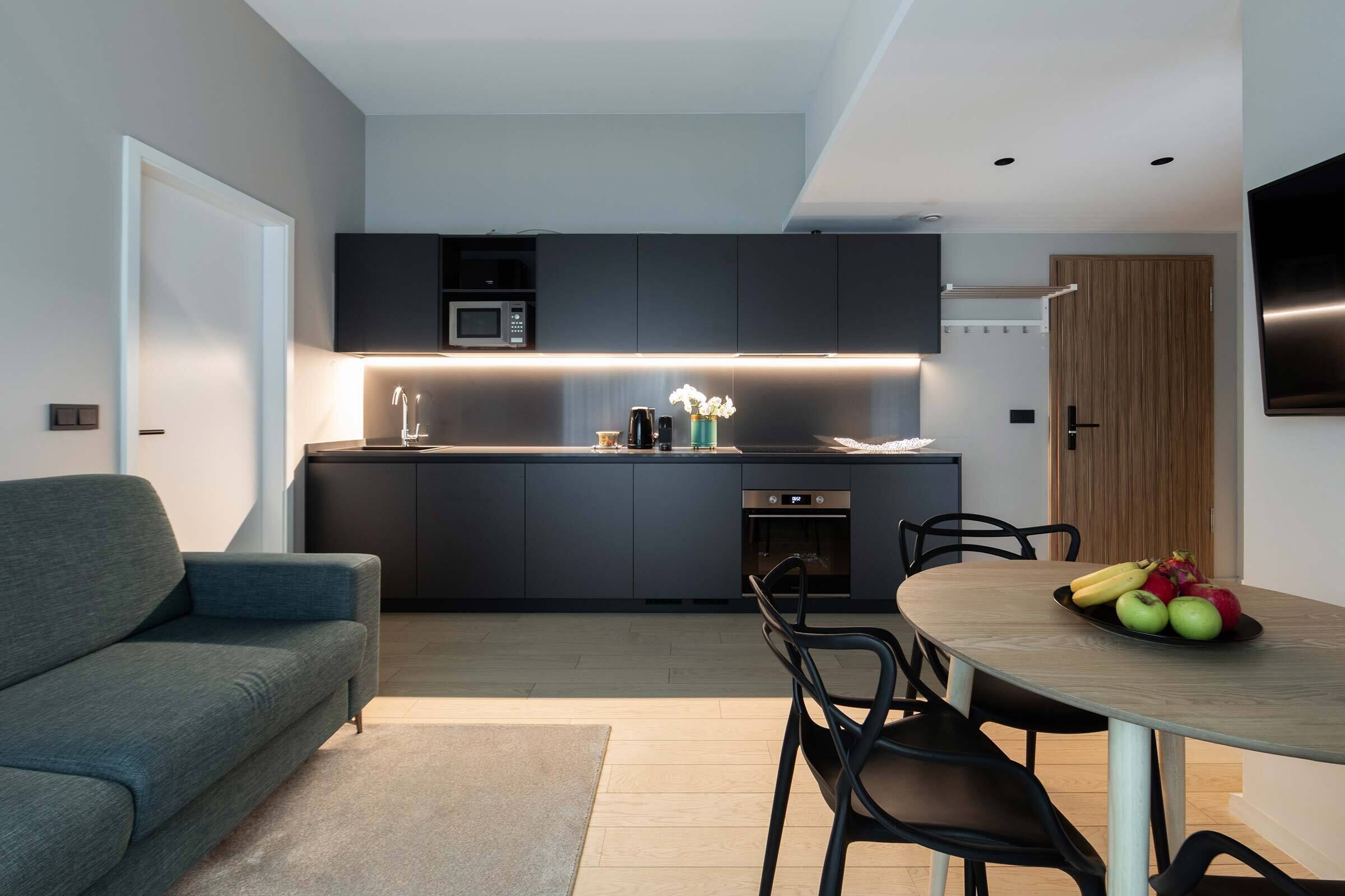 A modern kitchen with dark cabinetry, a built-in microwave, and a dining area with a round table and chairs.