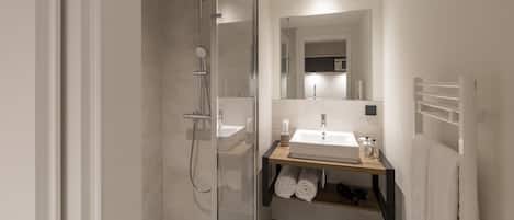Un baño moderno con ducha de vidrio, lavamanos con espejo y perchero.