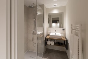 Un baño moderno con ducha de vidrio, lavamanos con espejo y perchero.