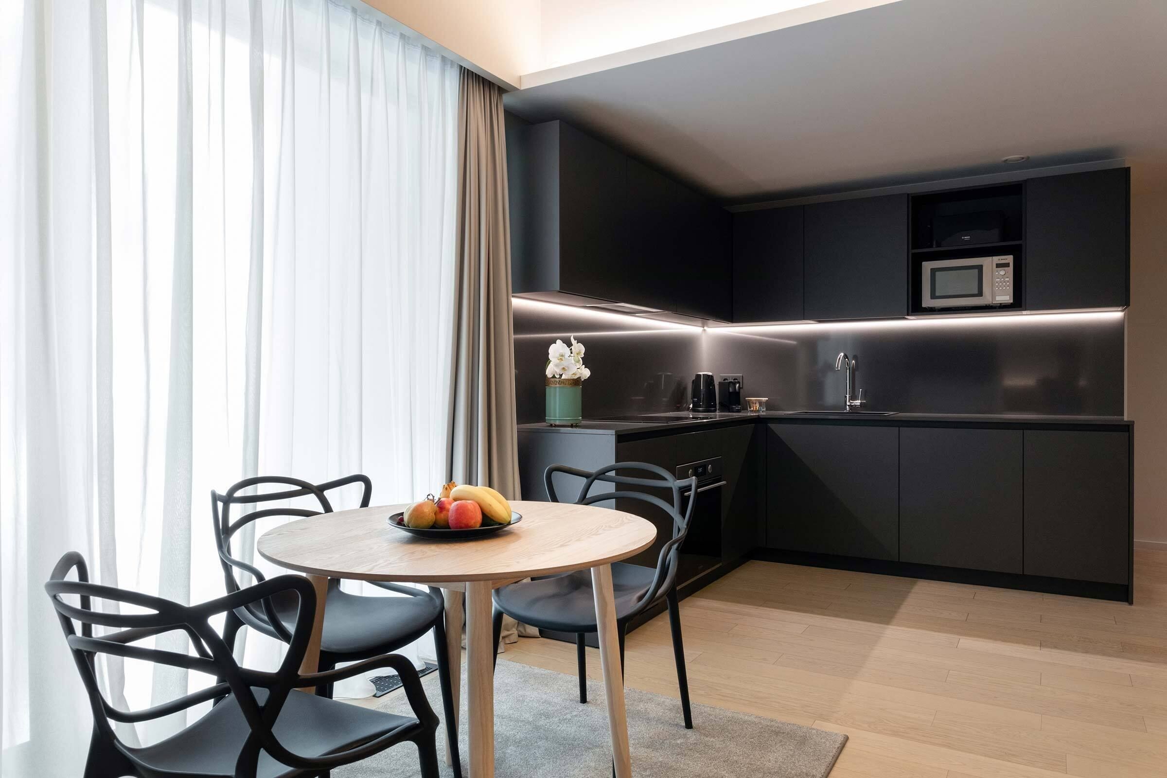 A modern kitchen with dark cabinetry, a microwave, and a small dining area with a round table and chairs.
