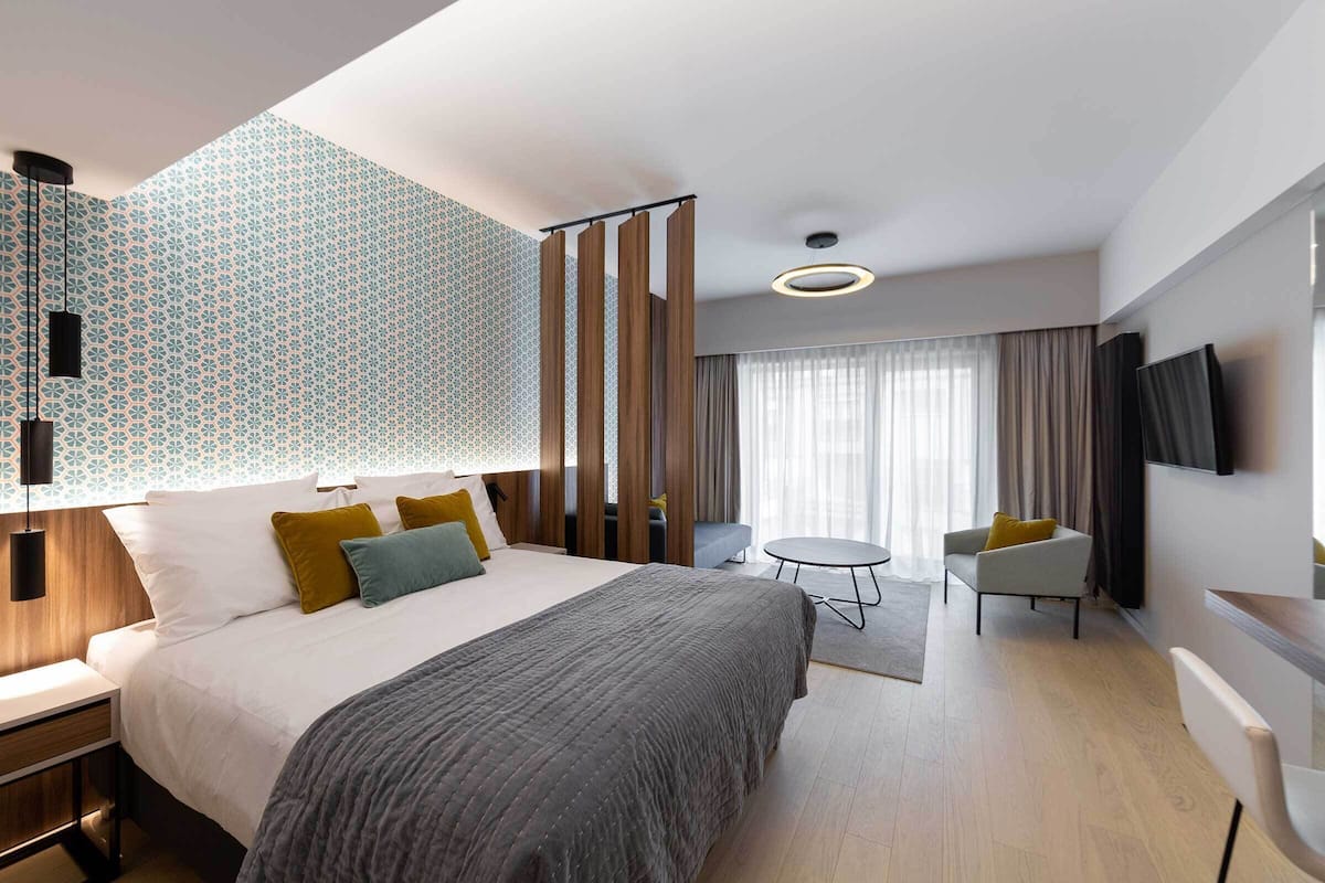 A modern hotel room with a large bed, a desk, a chair, a TV, and a window with curtains.