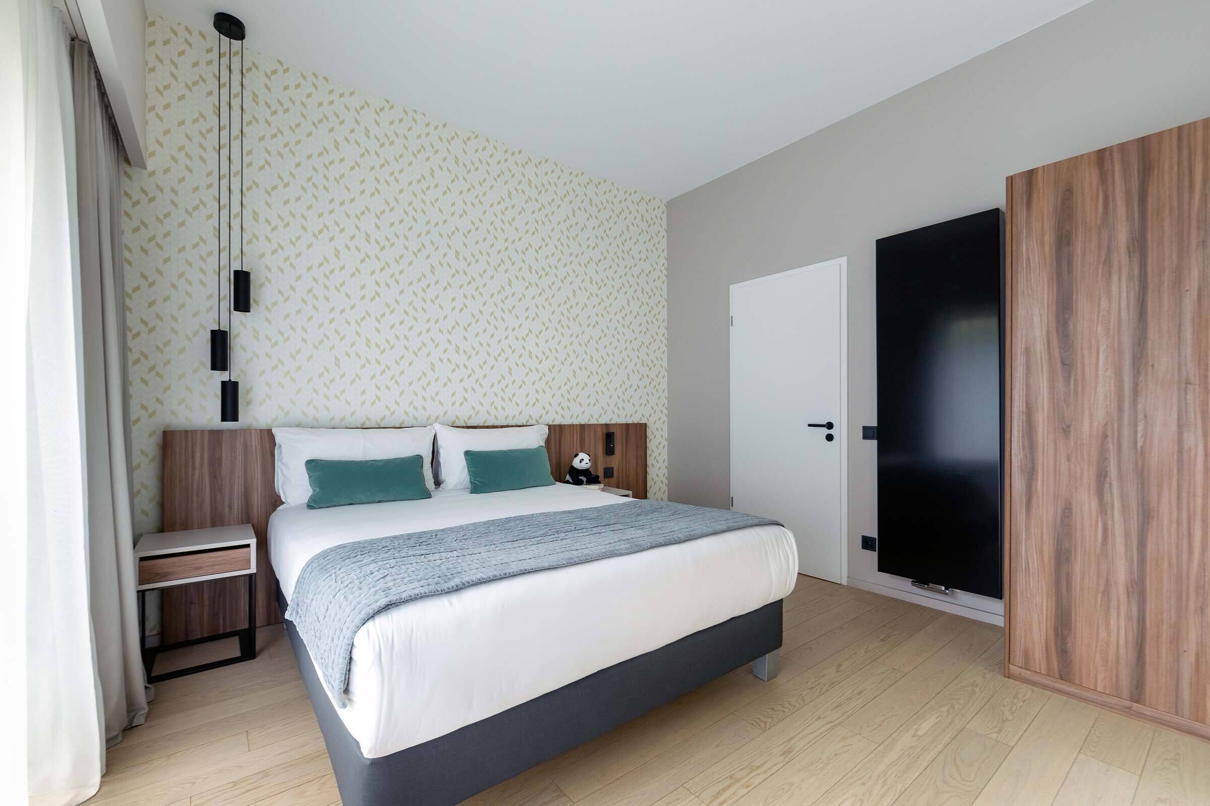 A modern bedroom with a bed, bedside tables, a wardrobe, and a hanging light fixture.