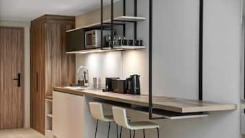 A modern kitchen with a wooden cabinet, a microwave, a coffee maker, and two bar stools.