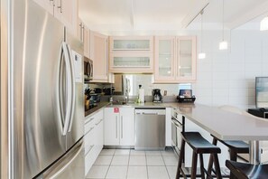 A modern kitchen with stainless steel appliances, white cabinetry, and a central island with stools.