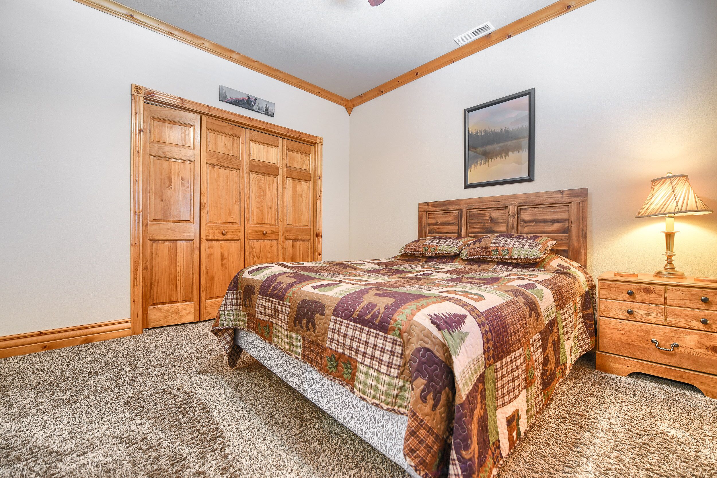 A bedroom with a large bed, wooden wardrobe, and a nightstand with a lamp.