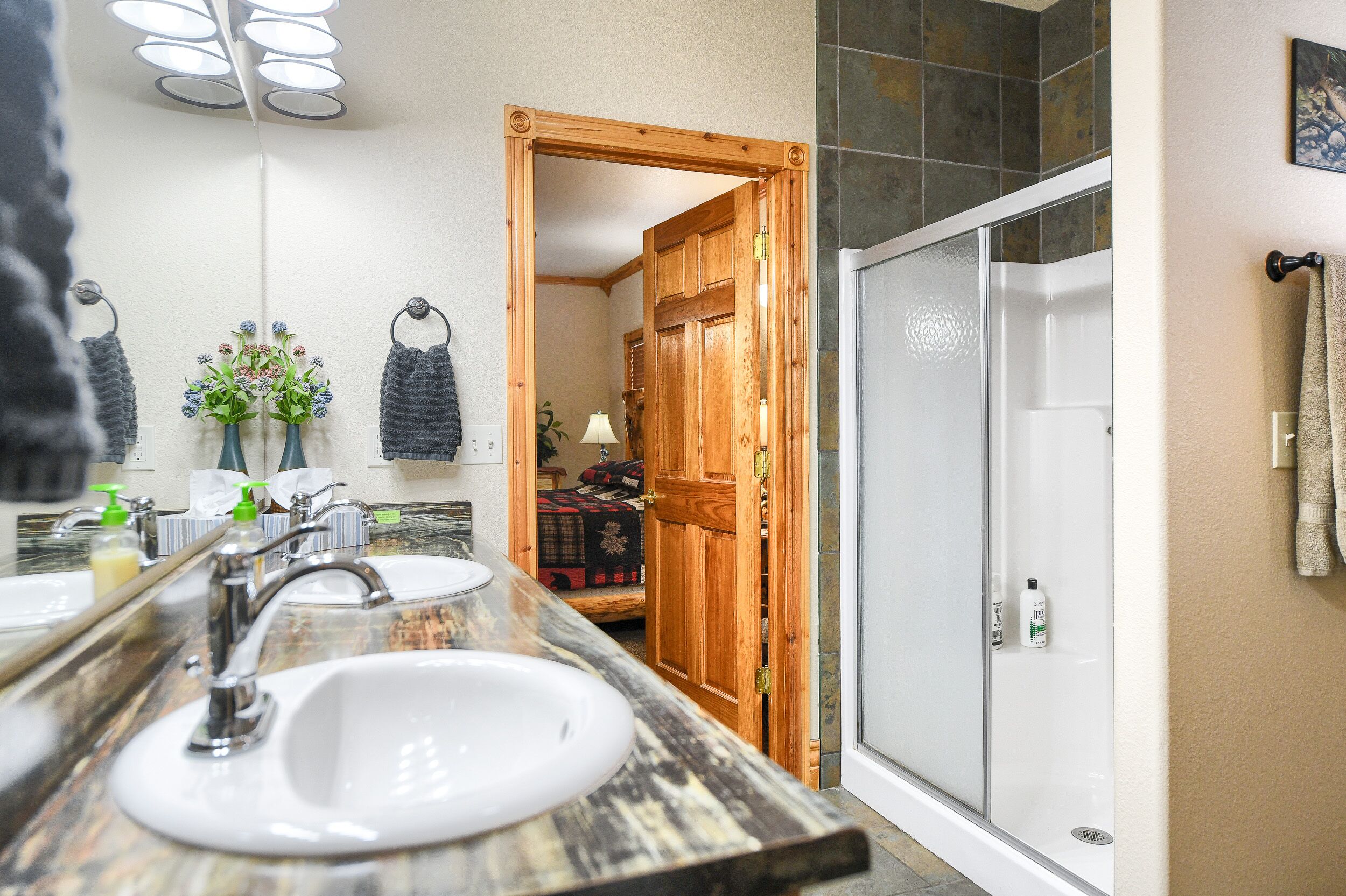 A bathroom with a wooden door, a shower, and a sink with a mirror.
