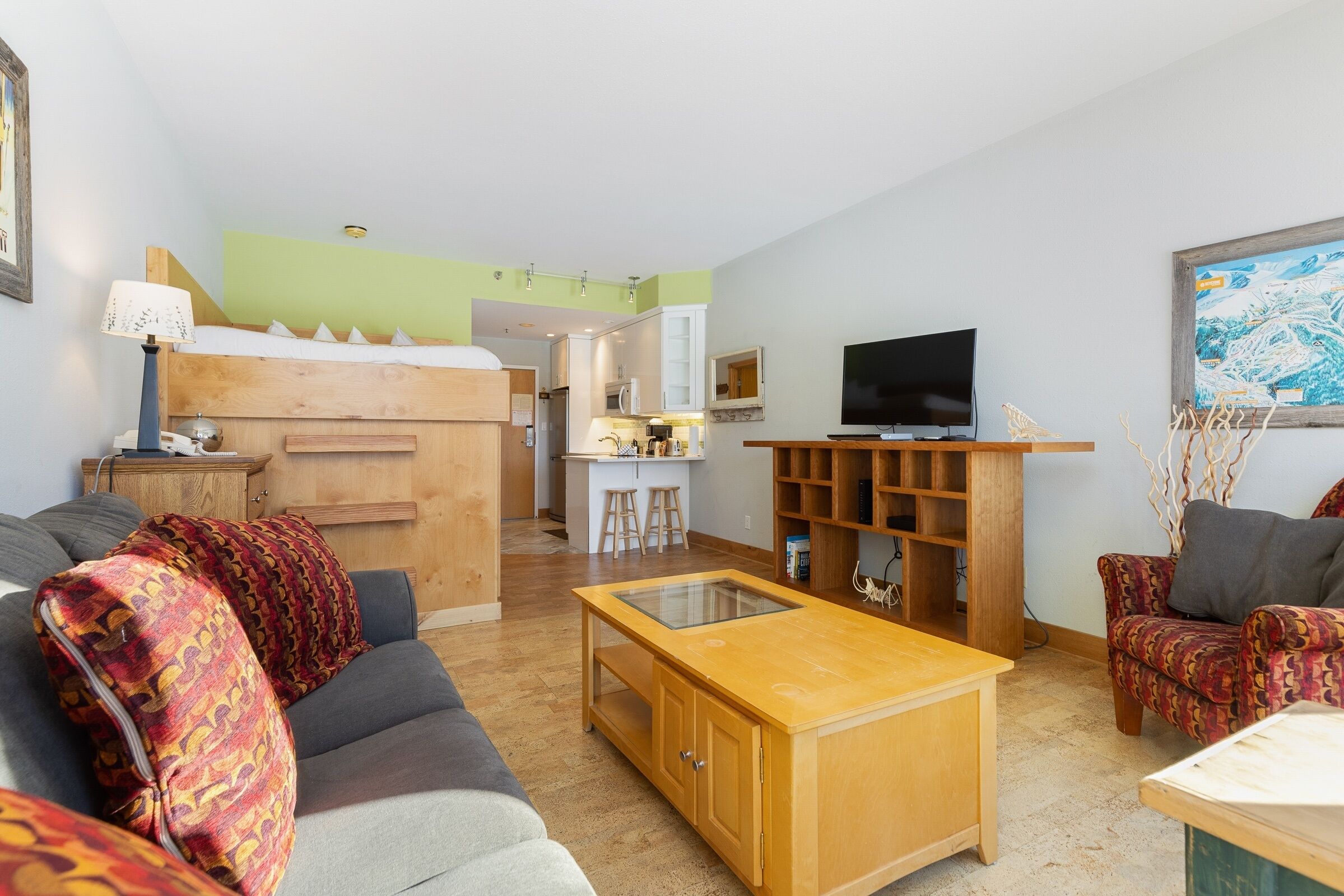A modern living room with a sofa, a coffee table, and a TV. There is a kitchen area with a fridge and a microwave.