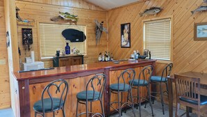 Um quarto com painéis de madeira, área de bar, banquetas e uma mesa de jantar.